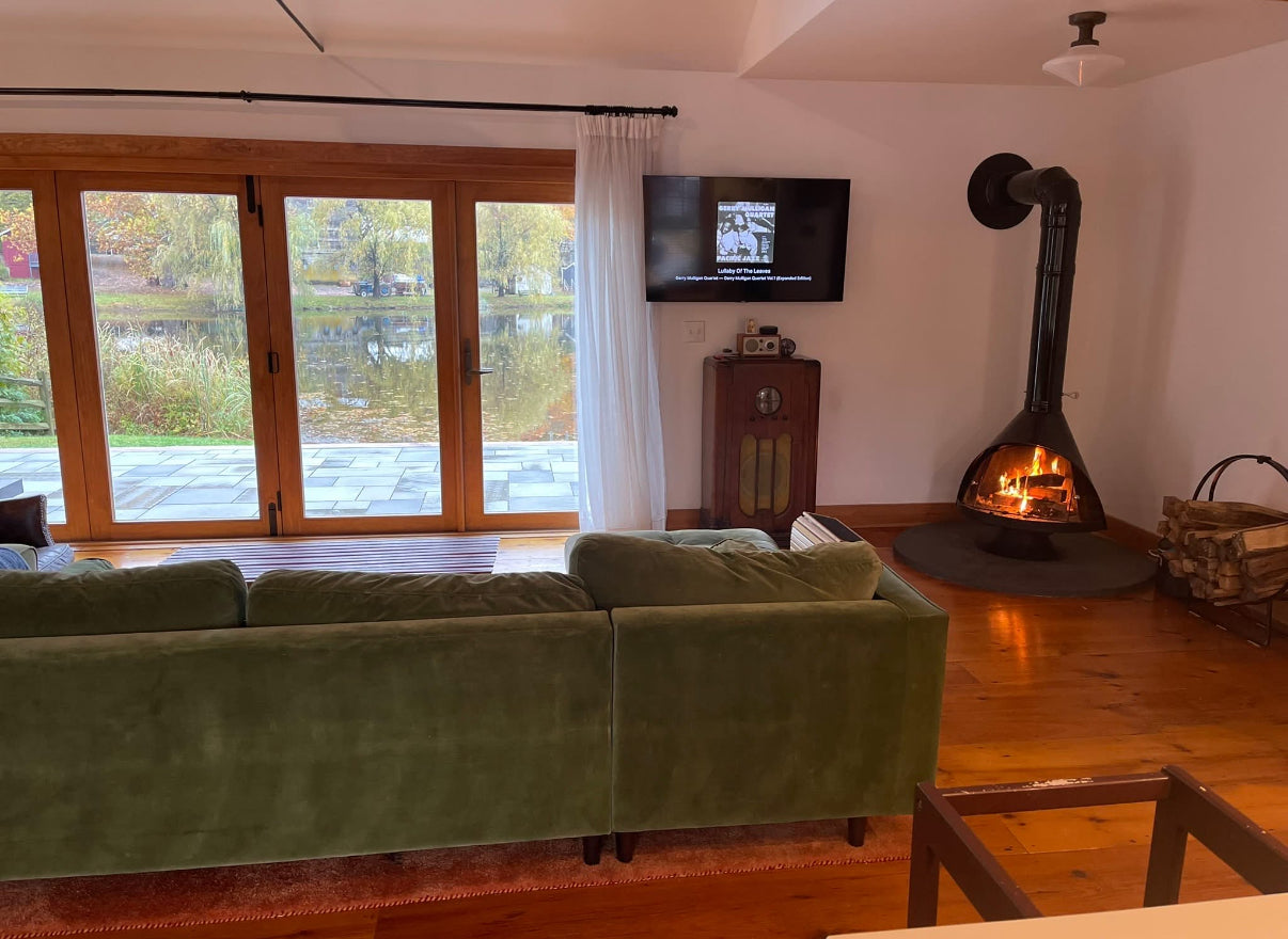 Living room with green sofa, fireplace, and television. Mid-century modern Malm Zircon fireplace installed in designer living room – premium Malm wood-burning fireplace available from Smokey Mountain Fireplaces.