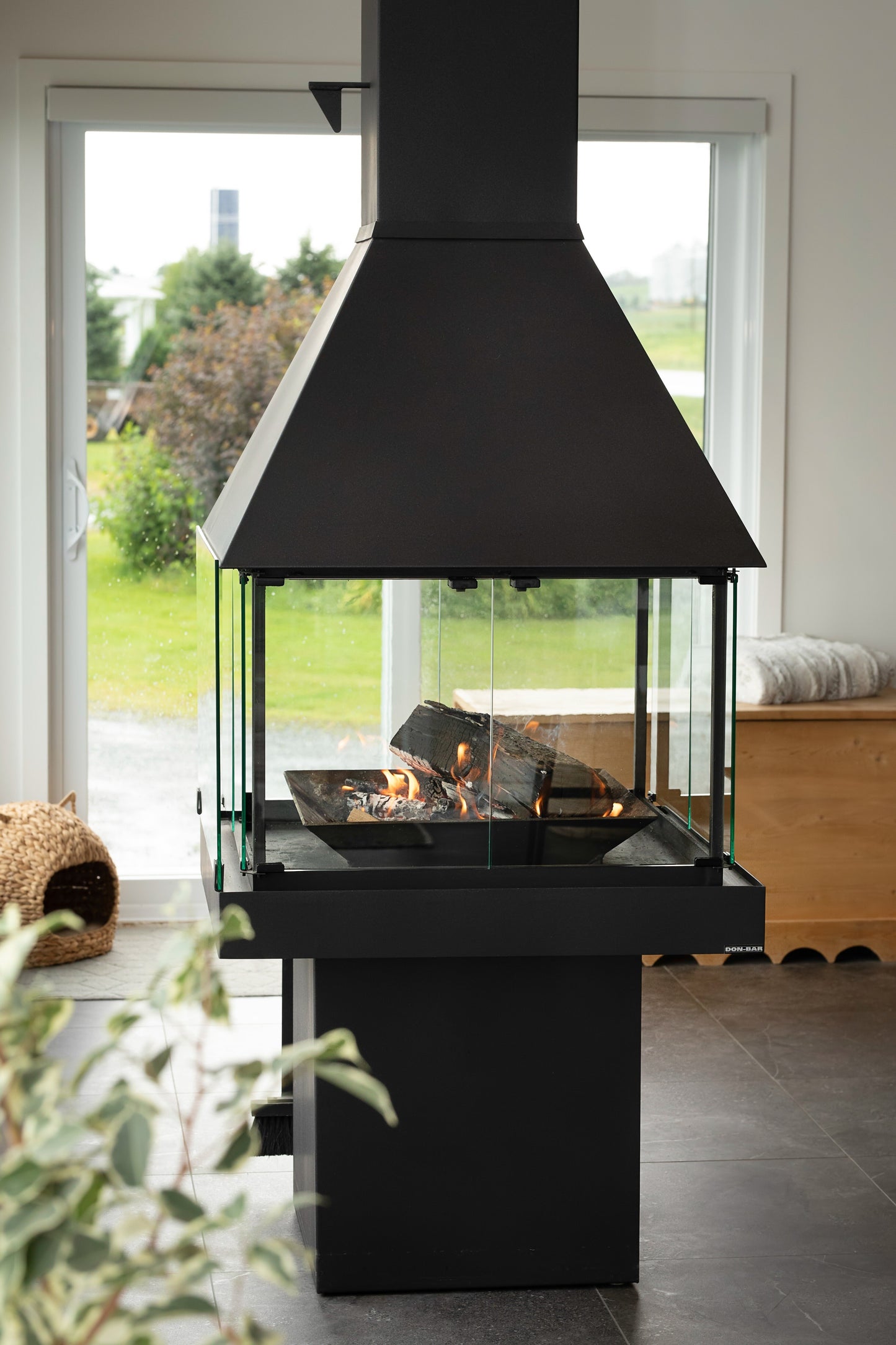 Modern outdoor  matte black don bar 9200 series fireplace with black hood and glass panels, set against a blurred natural background.