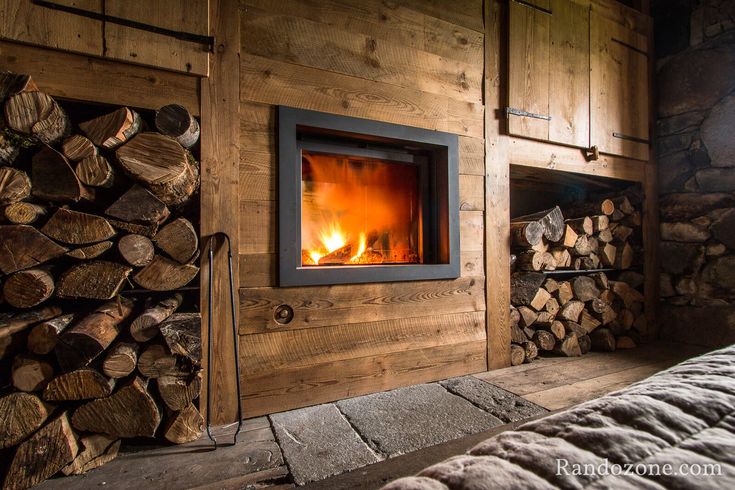 picture type frame Stuv 21-95DF in a Wooden wall with burning logs and stacked firewood on a rustic wall.