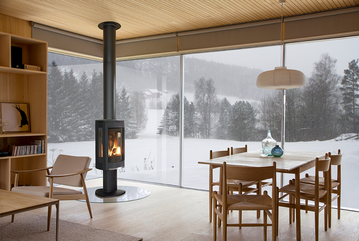 Modern interior with a Matte Black GF 370 DV Gas Stove, dining table, and chairs by large windows with a snowy landscape view.