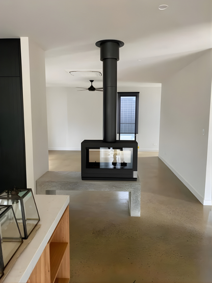 Invicta Aaron Double sided Glass 36" Cast Iron wood burning stove in a middle of a living room.