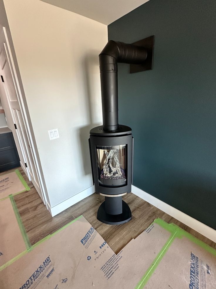 Matte Black freestanding Jotul GF 370 DV IPI Gas stove in a room and Elbow Chimney Vent to a dark green wall and cardboard on the floor.