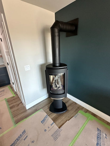 Matte Black freestanding Jotul GF 370 DV IPI Gas stove in a room and Elbow Chimney Vent to a dark green wall and cardboard on the floor.
