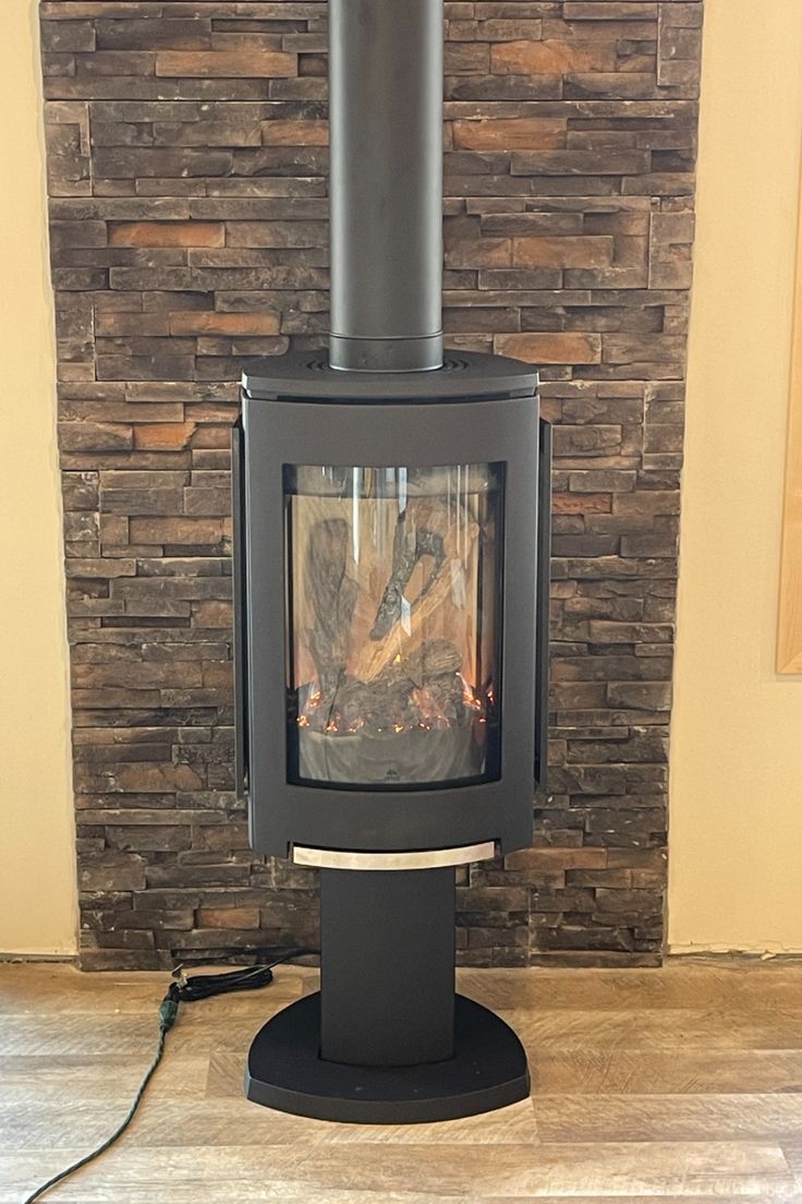 Matte Black freestanding Jotu GF 370 DV IPI Gas Stove against a stone wall.