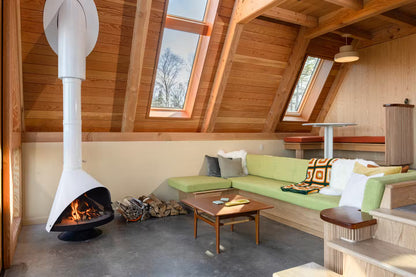 Modern living room with a white coated Top Finish and Matte Black Base Finish Cone shape Malm 30" zircon wood burning fireplace and  green sofa, and wooden table.