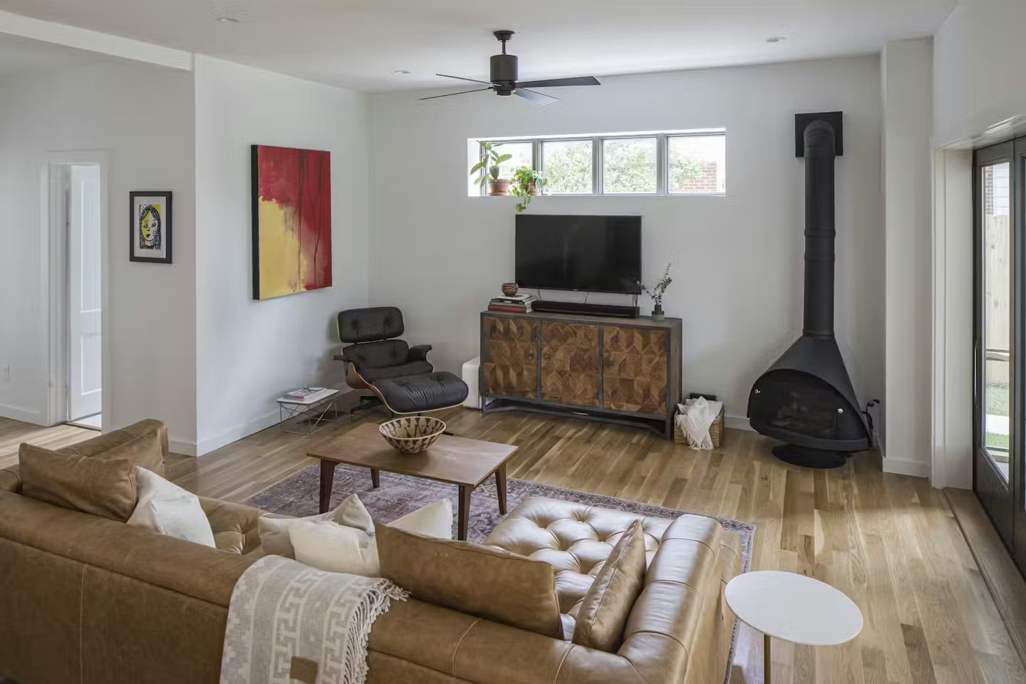 Matte Black Top Finish and a Matching Base Malm 30" Zircon Wood Burning Fireplace in Living room with brown sofa, wooden coffee table, and television on a wooden cabinet.