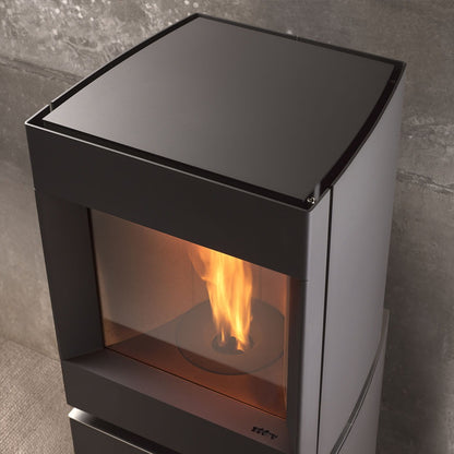 Black Overhead head view of steel base free standing Stuv S-P10 pellet stove with visible burning flame in a modern living room. Modern Indoor remote control and Smart phone control Home heating fireplace. Eco-Friendly, Gentle flame Indoor fireplace. This Fireplace is similar to ComfortBilt Alpine HP40 Pellet Stove, Osburn Volta Pellet Stove, Quadra-Fire Outfitter II Pellet Stove Display Demo,US Stove 1300 Sq ft Wood Pellet Stove, Castle | Serenity Pellet Stove.