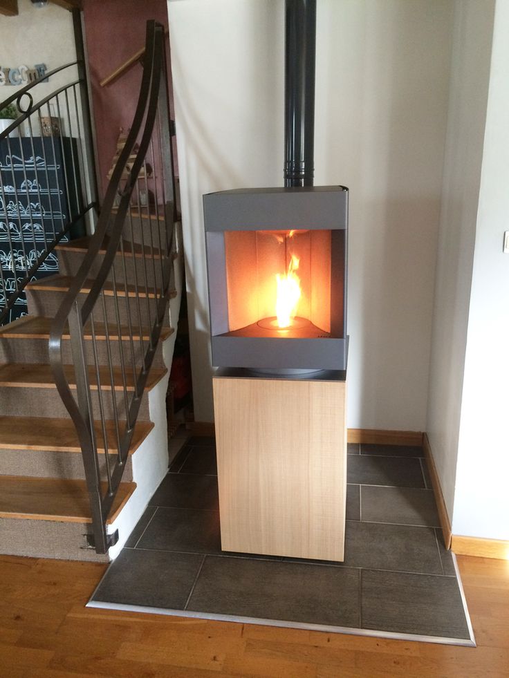Bleach oak base free standing Stuv S-P10 pellet stove with a visible burning flame in a corner of a modern living room. Modern Indoor remote control and Smart phone control Home heating fireplace. Eco-Friendly, Gentle flame Indoor fireplace. This Fireplace is similar to ComfortBilt Alpine HP40 Pellet Stove, Osburn Volta Pellet Stove, Quadra-Fire Outfitter II Pellet Stove Display Demo,US Stove 1300 Sq ft Wood Pellet Stove, Castle | Serenity Pellet Stove.