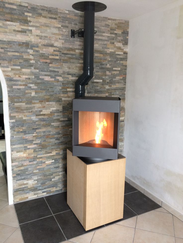 Bleach oak base free standing Stuv S-P10 pellet stove with visible burning flame in a corner of a modern living room. Modern Indoor remote control and Smart phone control Home heating fireplace. Eco-Friendly, Gentle flame Indoor fireplace. This Fireplace is similar to ComfortBilt Alpine HP40 Pellet Stove, Osburn Volta Pellet Stove, Quadra-Fire Outfitter II Pellet Stove Display Demo,US Stove 1300 Sq ft Wood Pellet Stove, Castle | Serenity Pellet Stove.