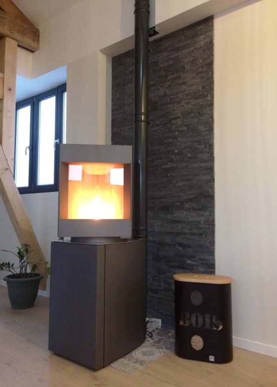 pivot head dark oak base free standing Stuv S-P10 pellet stove with visible burning flame in a corner of a modern living room. Modern Indoor remote control and Smart phone control Home heating fireplace. Eco-Friendly, Gentle flame Indoor fireplace. This Fireplace is similar to ComfortBilt Alpine HP40 Pellet Stove, Osburn Volta Pellet Stove, Quadra-Fire Outfitter II Pellet Stove Display Demo,US Stove 1300 Sq ft Wood Pellet Stove, Castle | Serenity Pellet Stove.