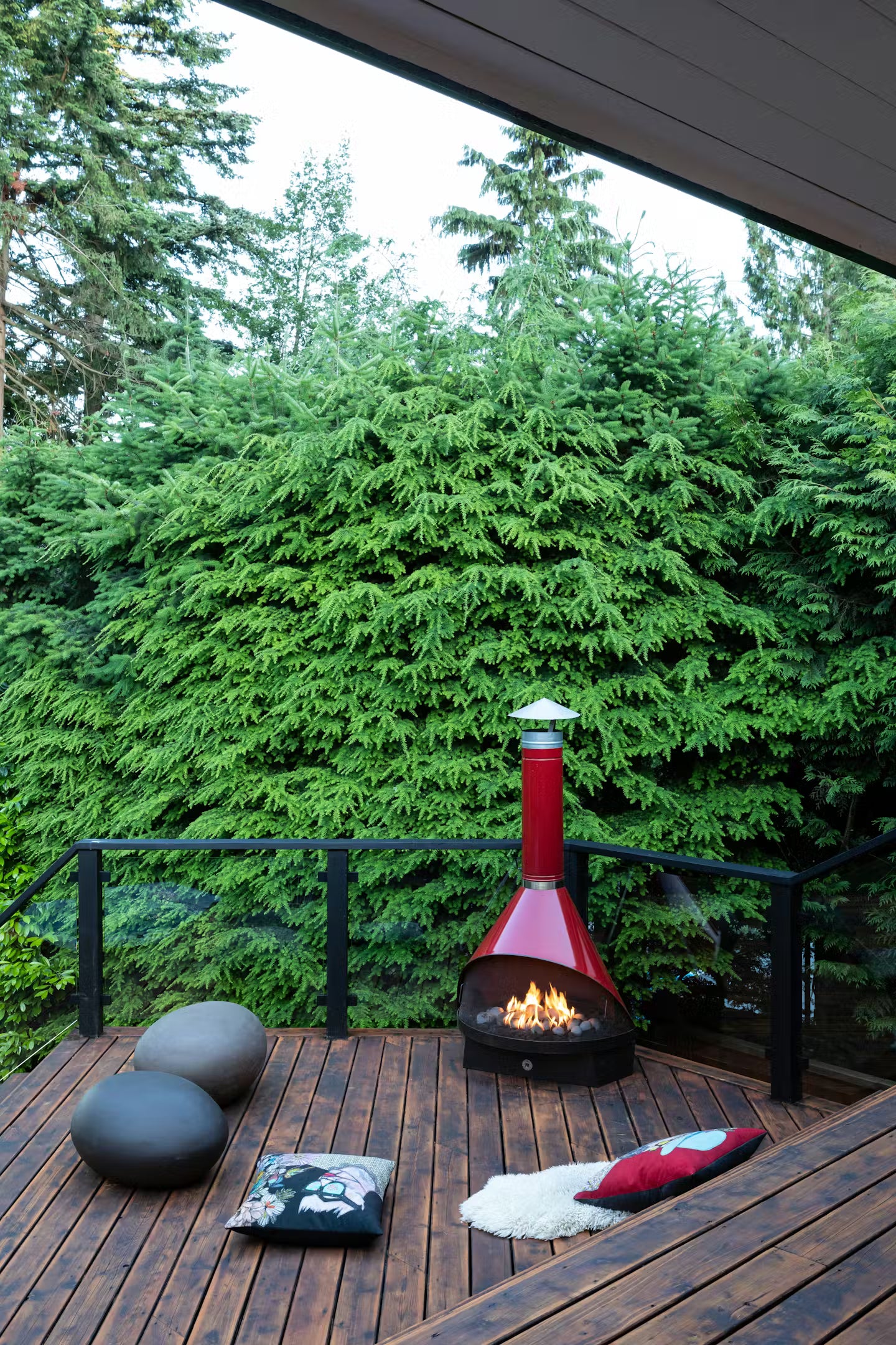 Outdoor View of Red Coated Top Finish and Matte Black Base Finish Cone shape Malm 30" zircon wood burning fireplace  on a wooden deck with green trees in the background.