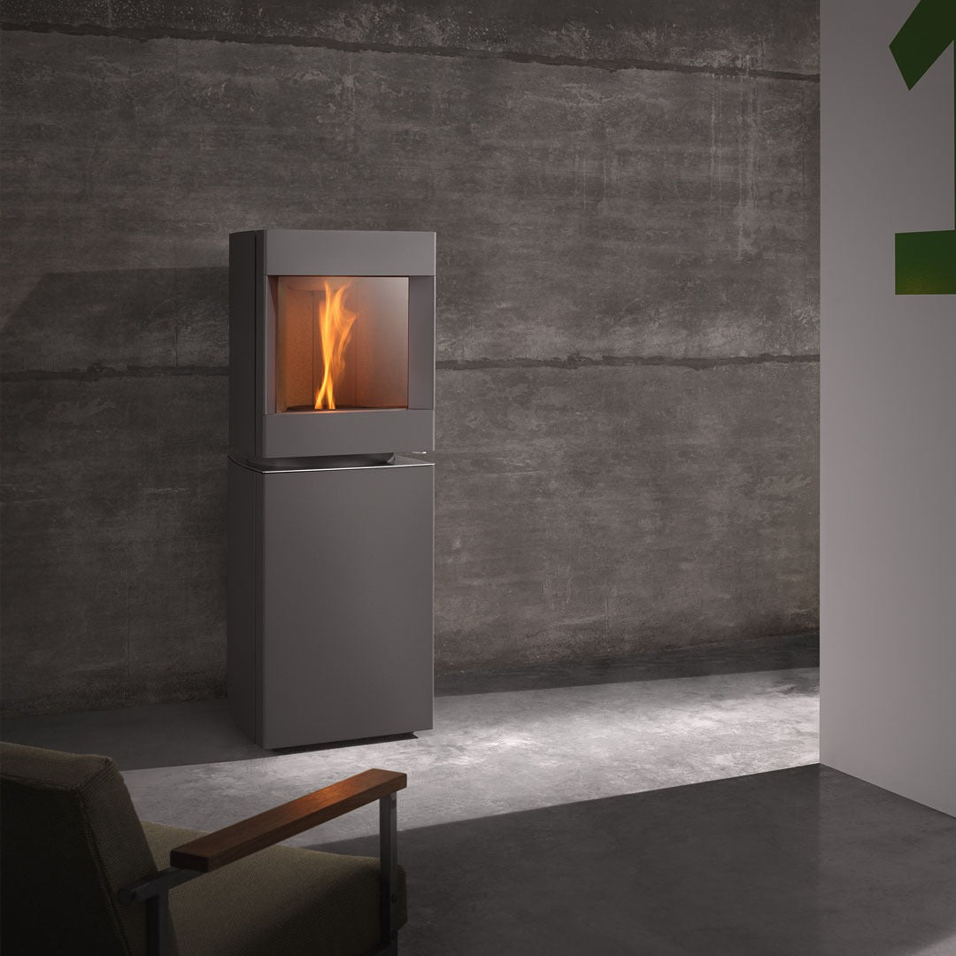 Steel Base free standing Stuv S-P10 pellet stove with visible burning flame in a modern living room. Modern Indoor remote control and Smart phone control Home heating fireplace. Eco-Friendly, Gentle flame Indoor fireplace. This Fireplace is similar to ComfortBilt Alpine HP40 Pellet Stove, Osburn Volta Pellet Stove, Quadra-Fire Outfitter II Pellet Stove Display Demo,US Stove 1300 Sq ft Wood Pellet Stove, Castle | Serenity Pellet Stove.