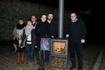 People stading with grey Stuv 16-H model wood burning stove with burning woods