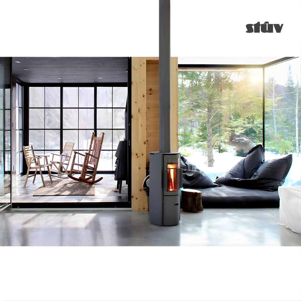 Stuv 30C Grey freestanding Premium and compact Wood Burning stove in a Modern living room with large windows and a rocking chairs. Top rated Indoor Log burner Fireplace with chimney connected to the roof.  Reduce Carbon Footprint with Wood-burning stove STUV 30C from Smokey Mountain Fireplaces With its high-quality steel construction, Multi-Use Function and wide range BTU heat Output.