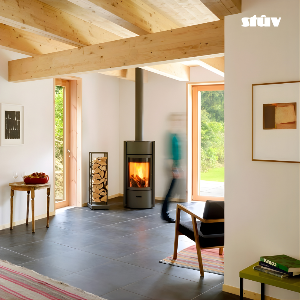 Grey Stuv 30C Freestanding highly efficient 360 degree rotating modern wood burning stove with visible flame  and a large log rack positioned at a corner of a living room with large windows, chair and wooden beams.
Premium and compact Indoor log burner fireplace with high-quality steel construction, Multi-Use Function and wide range BTU heat Output. 
Reduce carbon footprint with Stuv 30C wood stove from Smokey Mountain Fireplace, Eco-friendly and Best for the money fireplace.