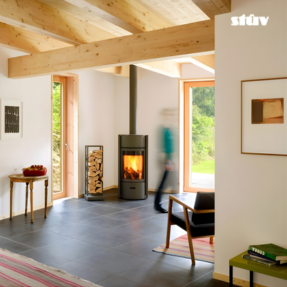 Grey Stuv 30C Freestanding highly efficient 360 degree rotating modern wood burning stove with visible flame  and a large log rack positioned at a corner of a living room with large windows, chair and wooden beams.
Premium and compact Indoor log burner fireplace with high-quality steel construction, Multi-Use Function and wide range BTU heat Output. 
Reduce carbon footprint with Stuv 30C wood stove from Smokey Mountain Fireplace, Eco-friendly and Best for the money fireplace.