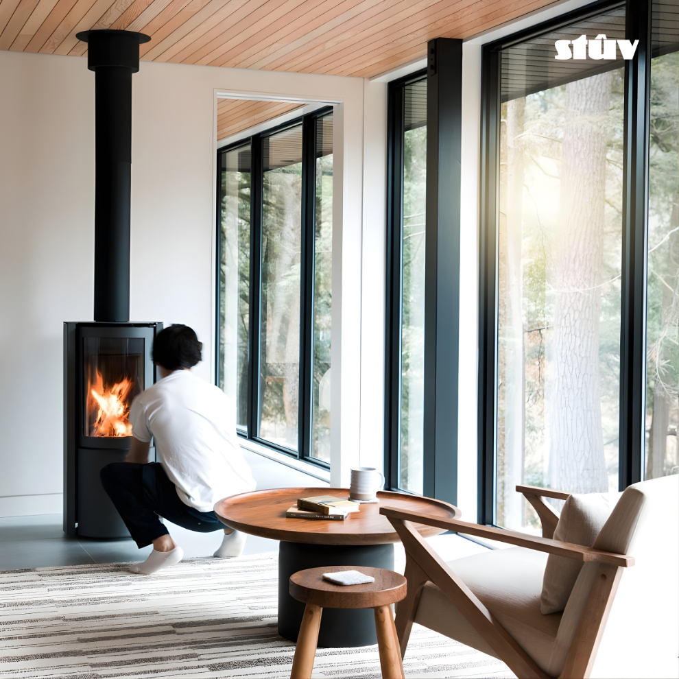 A man wearing White shirt sitting by Stuv 30C wood burning fireplace and stove with a Black Chimney connected to the roof in a room with large windows and a wooden chair. Experience Soulful Simplicity: The Stûv 30-Compact
Transform your living space into a minimalist home sanctuary. The Stûv 30-C isn't just a heater; it’s a functional piece of art. Designed with the 2026 Japandi style fireplace trend in mind, it blends Japanese zen with Scandinavian warmth, featuring a slender cylindrical body that saves sp