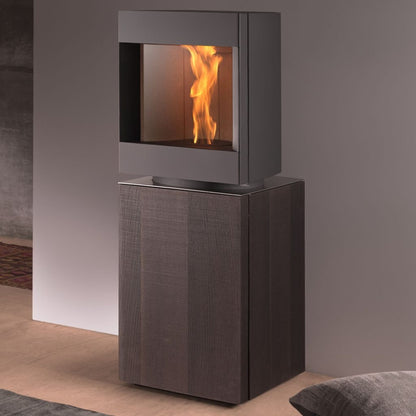 Dark oak base free standing Stuv S-P10 pellet stove with visible burning flame in amodern living room. Modern Indoor remote control and Smart phone control Home heating fireplace. Eco-Friendly, Gentle flame Indoor fireplace. This Fireplace is similar to ComfortBilt Alpine HP40 Pellet Stove, Osburn Volta Pellet Stove, Quadra-Fire Outfitter II Pellet Stove Display Demo,US Stove 1300 Sq ft Wood Pellet Stove, Castle | Serenity Pellet Stove.