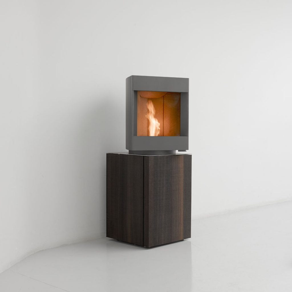 Custom Base free standing Stuv S-P10 pellet stove with visible burning flame in a modern living room. Modern Indoor remote control and Smart phone control Home heating fireplace. Eco-Friendly, Gentle flame Indoor fireplace. This Fireplace is similar to ComfortBilt Alpine HP40 Pellet Stove, Osburn Volta Pellet Stove, Quadra-Fire Outfitter II Pellet Stove Display Demo,US Stove 1300 Sq ft Wood Pellet Stove, Castle | Serenity Pellet Stove.