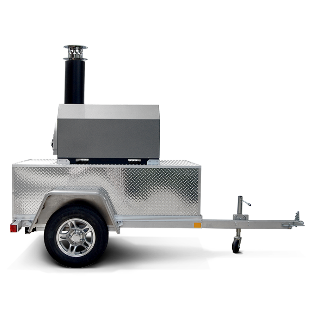 Side view of a wood-fired pizza oven trailer with a black oven on top and a silver metal base, mounted on a single-axle aluminum trailer, parked outdoors.