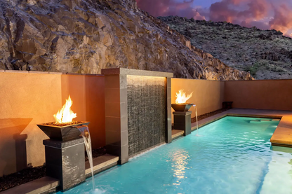 Luxury pool area with modern fire and water features at sunset, with a backdrop of rocky mountains