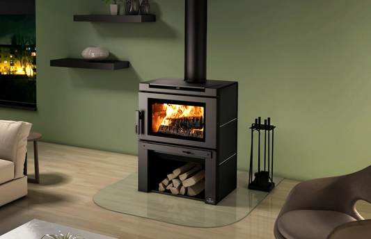 Black Top and Side Panel Osburn Matrix  Wood-burning stove with fire burning inside, logs stacked in the Firebox Underneath the stove, shelves and a green wall.