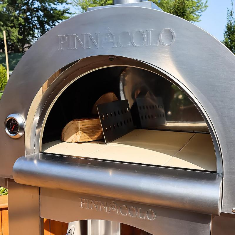 Pinnacolo wood-fired Stainless steel pizza oven with 'Pinnacolo' branding, showing open door with wood and spatula.