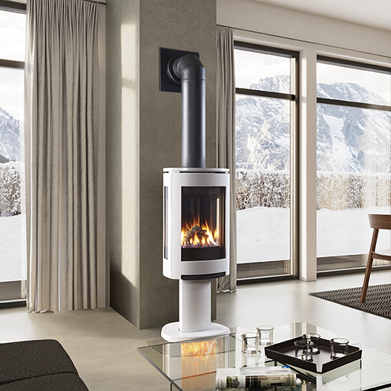 Modern Linen Color freestanding three sided GF Jotul 370 DV Gas stove in a living room with a Elbow Flue Pipe Direct Vent to the wall with  large windows showing a snowy landscape.