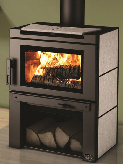 Soapstone Top and Side panel Osburn Matrix Wood-burning stove with fire burning inside, logs stacked in the Firebox Underneath the stove in a room setting.