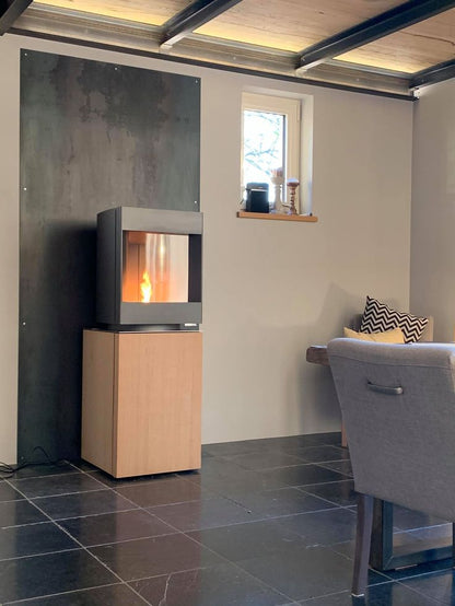 Bleach oak base free standing Stuv S-P10 pellet stove with a visbile burning flame in a modern living room. Modern Indoor remote control and Smart phone control Home heating fireplace. Eco-Friendly, Gentle flame Indoor fireplace. This Fireplace is similar to ComfortBilt Alpine HP40 Pellet Stove, Osburn Volta Pellet Stove, Quadra-Fire Outfitter II Pellet Stove Display Demo,US Stove 1300 Sq ft Wood Pellet Stove, Castle | Serenity Pellet Stove.