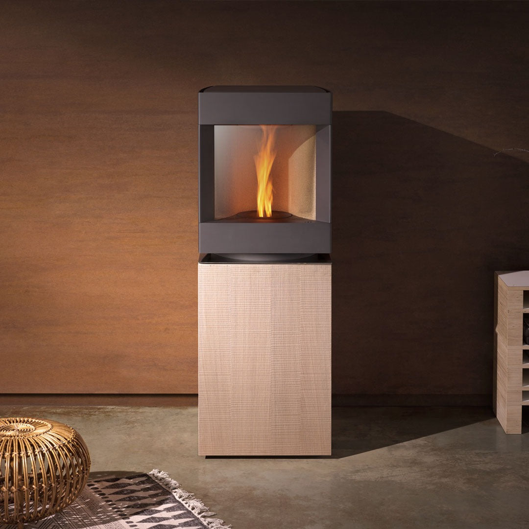 Bleached Oak Base Base free standing Stuv S-P10 pellet stove with visible burning flame in a modern living room. Modern Indoor remote control and Smart phone control Home heating fireplace. Eco-Friendly, Gentle flame Indoor fireplace. This Fireplace is similar to ComfortBilt Alpine HP40 Pellet Stove, Osburn Volta Pellet Stove, Quadra-Fire Outfitter II Pellet Stove Display Demo,US Stove 1300 Sq ft Wood Pellet Stove, Castle | Serenity Pellet Stove.